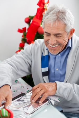 Happy senior man wrapping Christmas gift at homeの写真素材