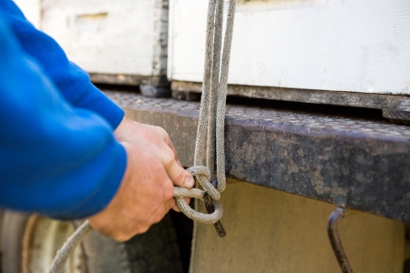 Closeup of beekeeper tying rope to hook of truck with honeycomb crates