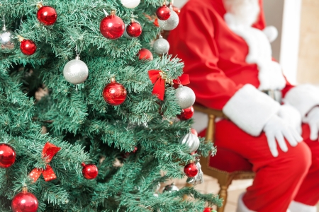 Closeup of decorated Christmas tree with Santa Claus sitting in background outdoorsの写真素材