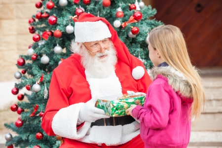 Santa Claus giving present to girl against Christmas treeの写真素材