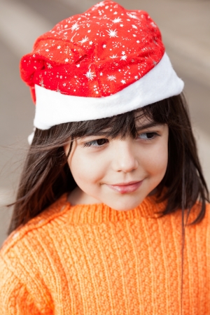 Cute girl in Santa hat looking away outdoorsの写真素材