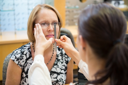 Female optician measuring mature woman's eyeglasses in storeの写真素材