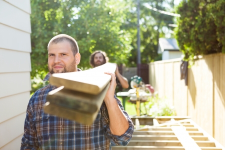 Portrait of male carpenter and coworker carrying lumbers at construction siteの写真素材