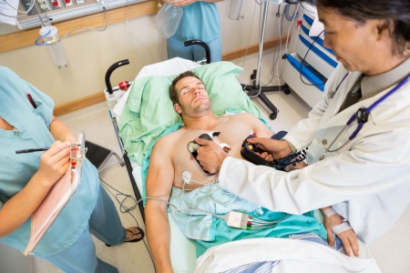 High angle view of doctor defibrillating male patient while nurses standing by in hospital