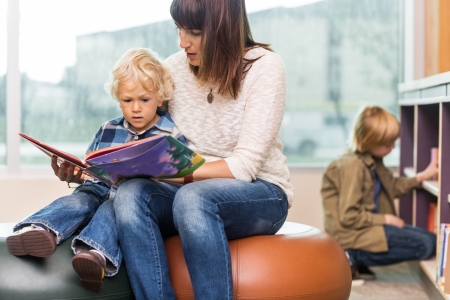 Young teacher with boy reading book in libraryの写真素材