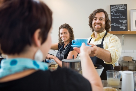 Happy barista serving customer cup of coffeeの写真素材