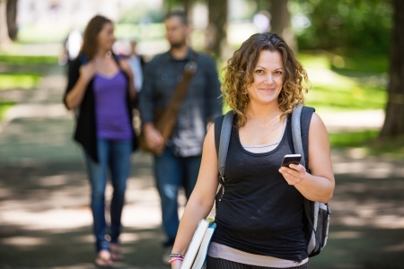 Portrait of female student with backpack holding cellphone while standing on campusの写真素材