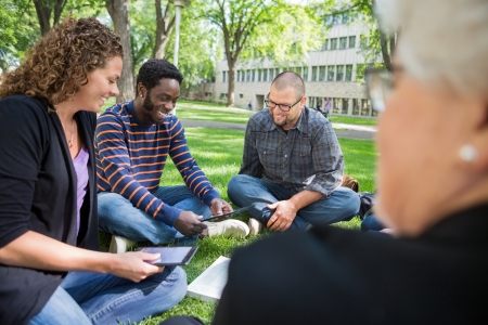 Group of multiethnic university students using digital tablet on campus parkの写真素材
