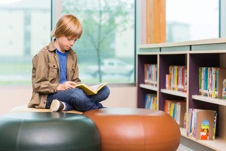 Young boy reading book in school libraryの写真素材