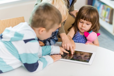 Cute girl with friends using digital tablet at table in school libraryの写真素材