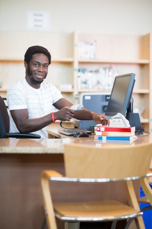 Portrait of young male librarian scanning books at desk in libraryの写真素材