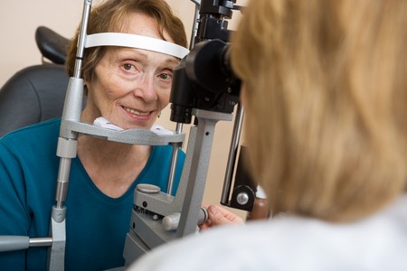 Portrait of senior woman having eye test with slit lamp in storeの写真素材