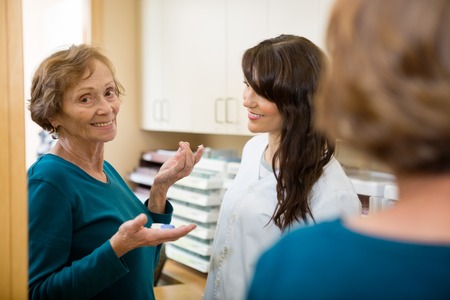 Optometrist looking at senior woman holding contact lens on finger in storeの写真素材