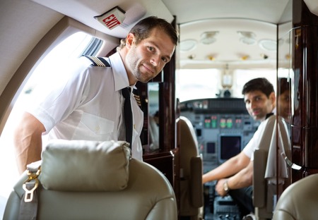Portrait of handsome pilot entering private jet with copilot in backgroundの写真素材