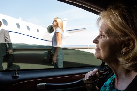 Thoughtful mature businesswoman in car looking at private jetの写真素材
