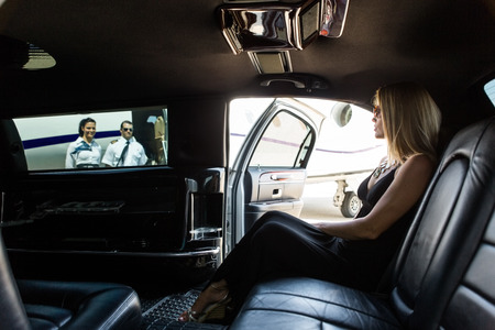 Elegant woman in limousine with airhostess and pilot near private jet at terminal Elegant woman in limousine with airhostess and pilot near private jet at terminal