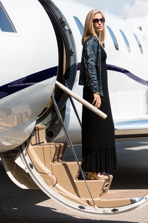 Full length of wealthy woman in elegant dress stepping out of private planeの写真素材