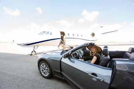 Portrait of woman disembarking car with private jet in background at terminal