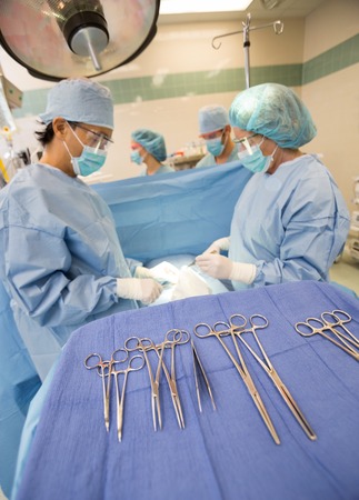 Surgical tools on stand with doctors operating patient in operation roomの写真素材
