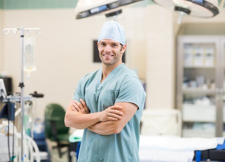 Portrait of happy male surgeon standing arms crossed in operation roomの写真素材