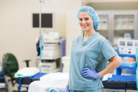 Portrait of beautiful surgeon with hand on hip standing in operation roomの写真素材