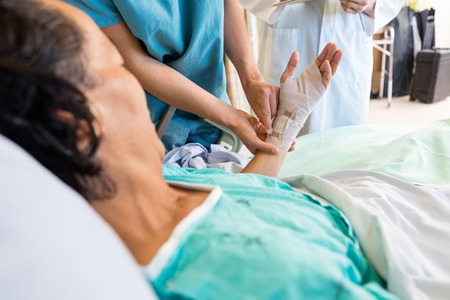 Midsection of nurse putting bandage on patient's hand while standing by doctor at hospitalの写真素材