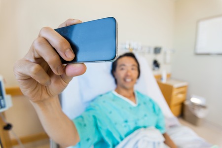 Male patient taking self portrait through mobile phone in hospitalの写真素材