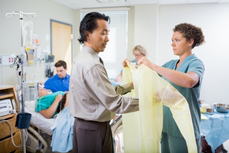Nurse assisting doctor in wearing operation gown with pregnant woman and man in backgroundの写真素材