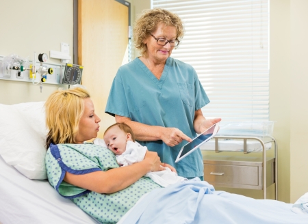 Mature female nurse explaining reports on digital tablet to woman with newborn babygirl in hospitalの写真素材