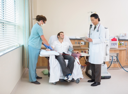 Full length of doctor using digital tablet with nurse giving renal dialysis to patient in hospital roomの写真素材