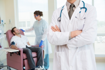 Midsection of male doctor standing arms crossed with nurse looking at patient being examined by pulse rate machine in hospitalの写真素材
