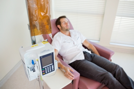 Male patient receiving chemotherapy through IV drip in hospital roomの写真素材