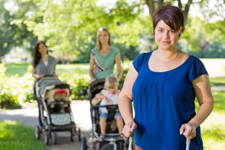 Portrait of mid adult mother holding baby stroller at park with friends 