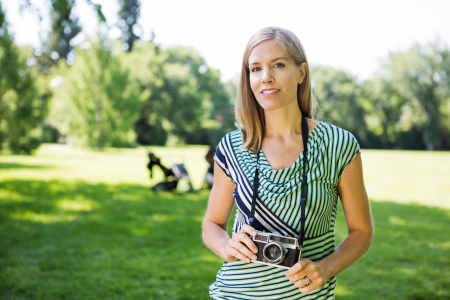 Portrait of happy mid adult woman with digital camera in parkの写真素材