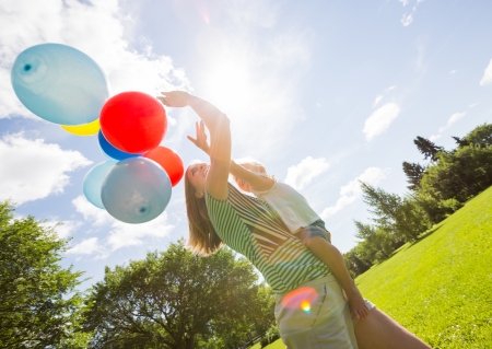 Side view of mother and daughter holding colorful balloons in parkの写真素材