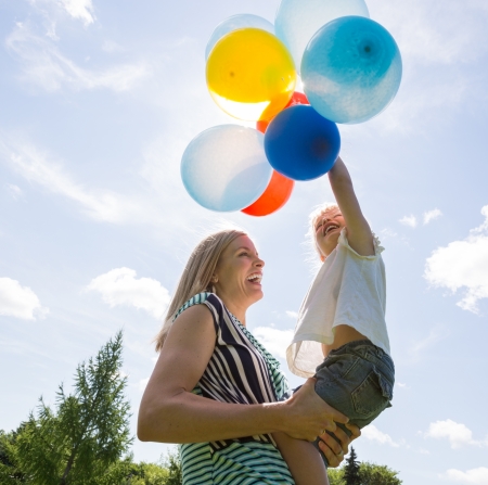 Cheerful mother and daughter playing with colorful balloons against cloudy skyの写真素材