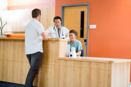 Doctor and nurse working at reception desk while patient standing in hospitalの写真素材