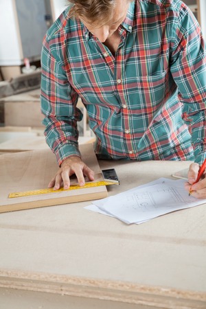 Carpenter Working On Blueprint While Measuring Woodの写真素材