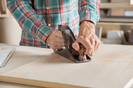 Midsection of male carpenter using planer on wood in workshopの写真素材