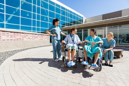 Patients On Wheelchair By Nurses Outside Hospital Buildingの写真素材