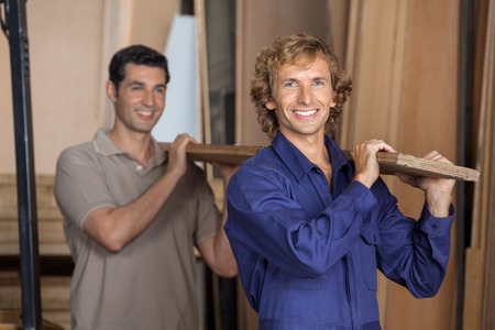 Carpenters Carrying Plank On Shoulders In Workshopの写真素材