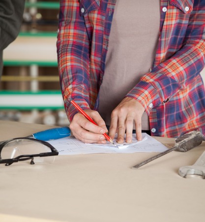 Midsection of worker drawing blueprint at table in workshopの写真素材