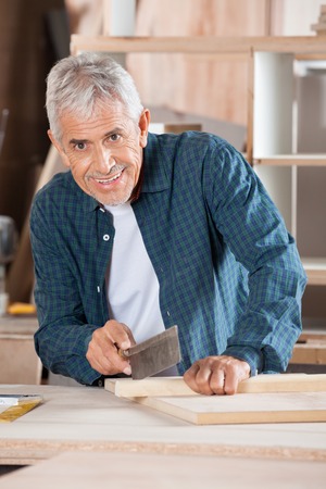 Portrait of senior man cutting wood with small saw at table in workshopの写真素材