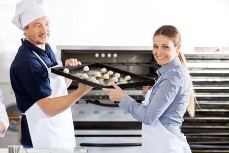 Happy Chef Giving Baking Sheet To Colleague In Kitchenの写真素材