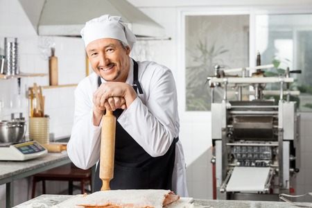 Happy Chef Holding Rolling Pin At Counter In Kitchenの写真素材