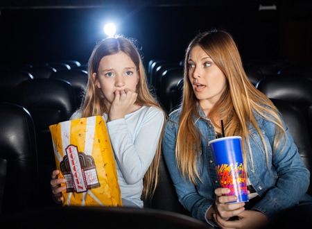 Woman Looking At Scared Daughter Watching Movieの写真素材