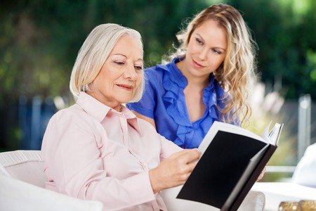 Granddaughter Looking At Grandmother Reading Bookの写真素材