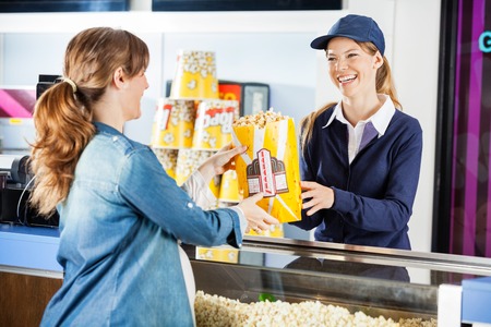 Happy Seller Giving Popcorn To Pregnant Woman At Concession Stanの写真素材