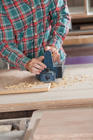 Midsection of worker using electric planer on wood at workshop