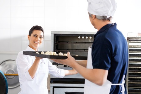 Smiling Chef Taking Baking Sheet From Colleague In Kitchenの写真素材